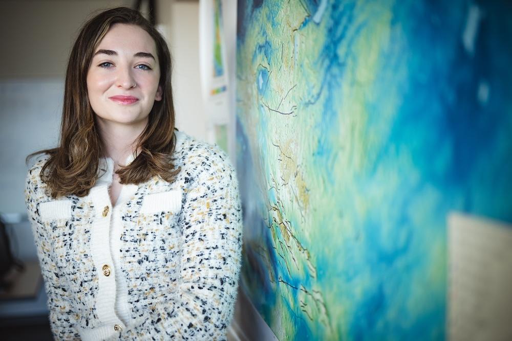 Rory Bertoldo poses for a portrait next to a topographical map